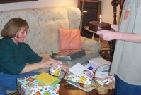 Kathy reaches for a gift while the birthday cake is presented.