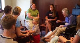 visitors seated around Great Grandma Turner, with Will standing in the center, holding his mother's hands