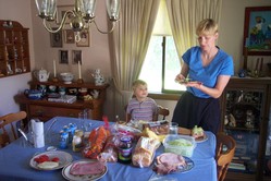 the dining room, with the table set with sandwich fixings, and DeeAnn preparing a sandwich for Will, who is standing by