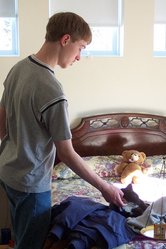 Phil standing beside a bed and petting a black and white cat, which is resting on a pile of coats