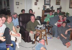 Grandpa in the easy chair with a slide projector, with eleven laughing onlookers